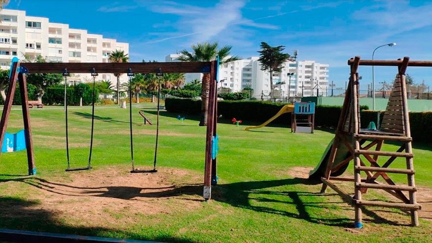 Parque infantil con un columpio y dos toboganes al costado de las pistas deportivas
